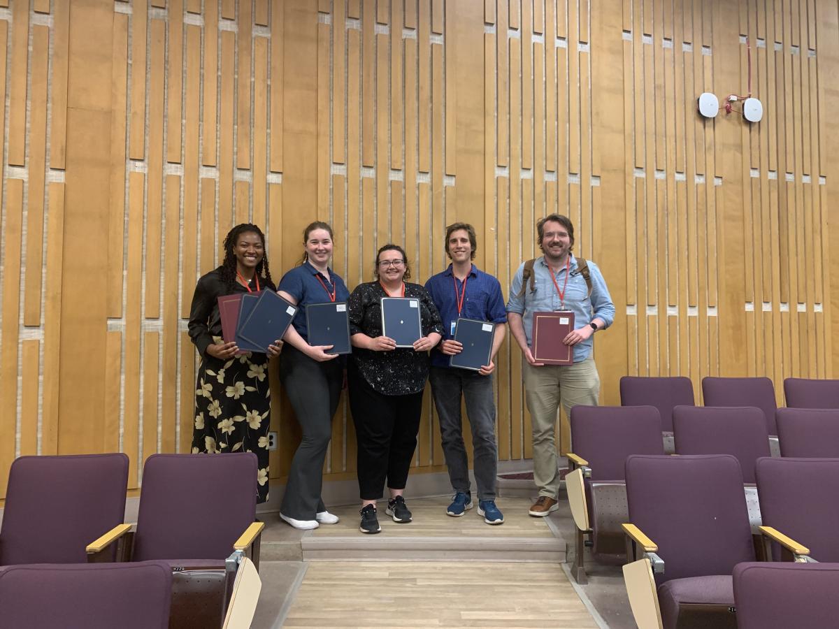 5 award winning students standing a lecture hall, holding folders